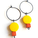 colorful yellow and red wooden beads hanging on a black creole by Pop-a-porter